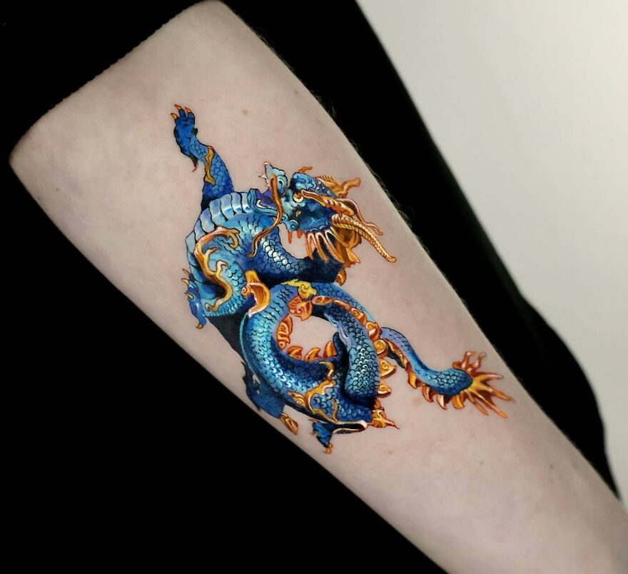 Blue and orange dragon tattoo design on a person's arm, showcasing detailed artistry and vibrant colors.