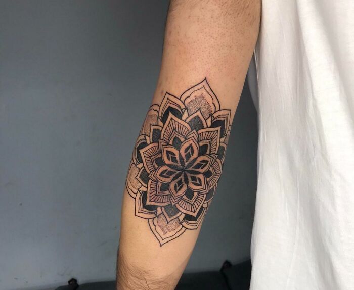 Intricate mandala elbow tattoo in black ink on a forearm, showcasing detailed geometric patterns.