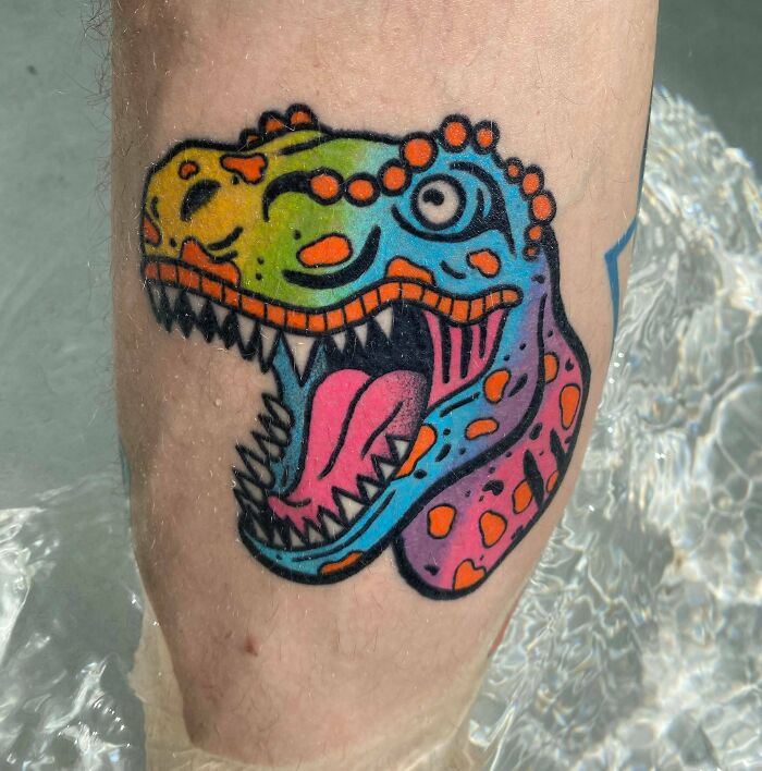 Colorful dinosaur elbow tattoo in vibrant hues, showcasing unique design elements and creativity.