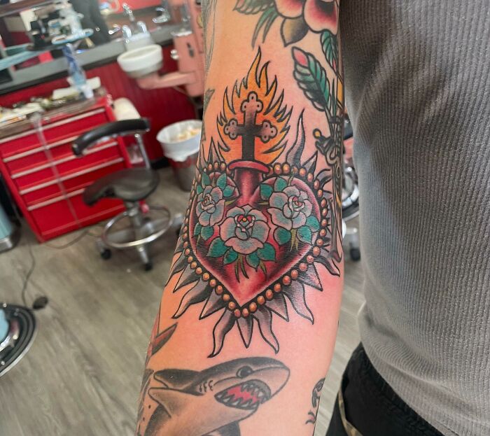 Elbow tattoo featuring a vibrant design with flowers and a burning heart, captured in a tattoo studio setting.
