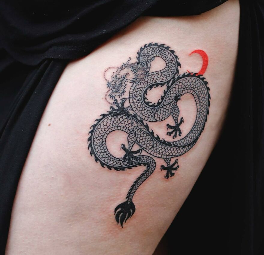 Detailed dragon tattoo design with a red crescent accent on a person's skin.