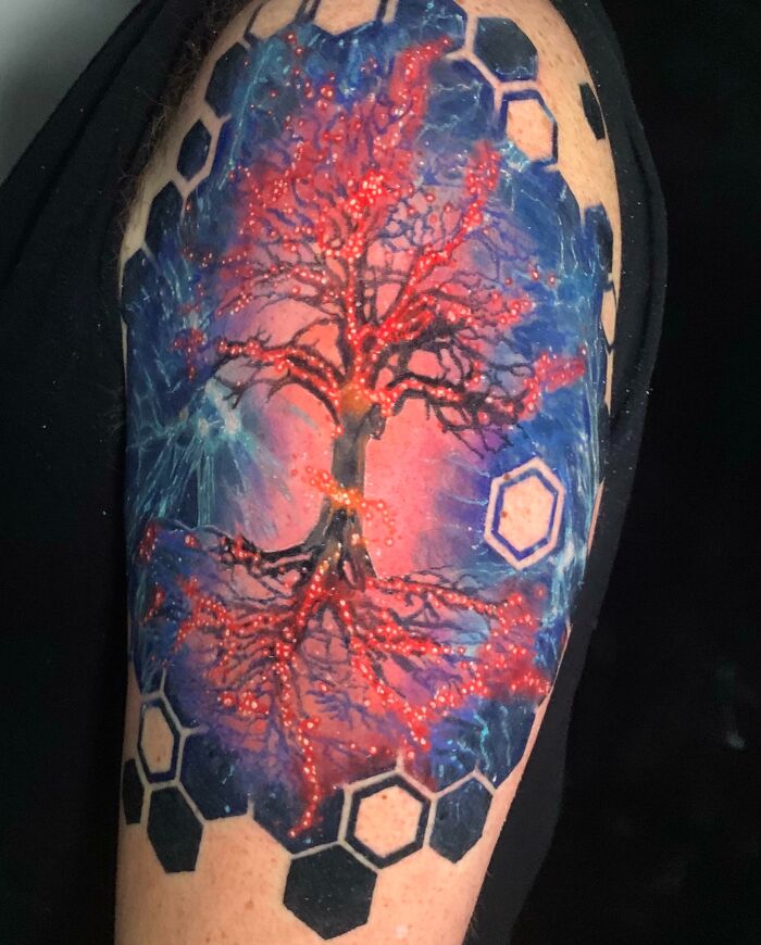 A colorful tree tattoo with cosmic background and geometric patterns on an arm, highlighting the wonders of nature.