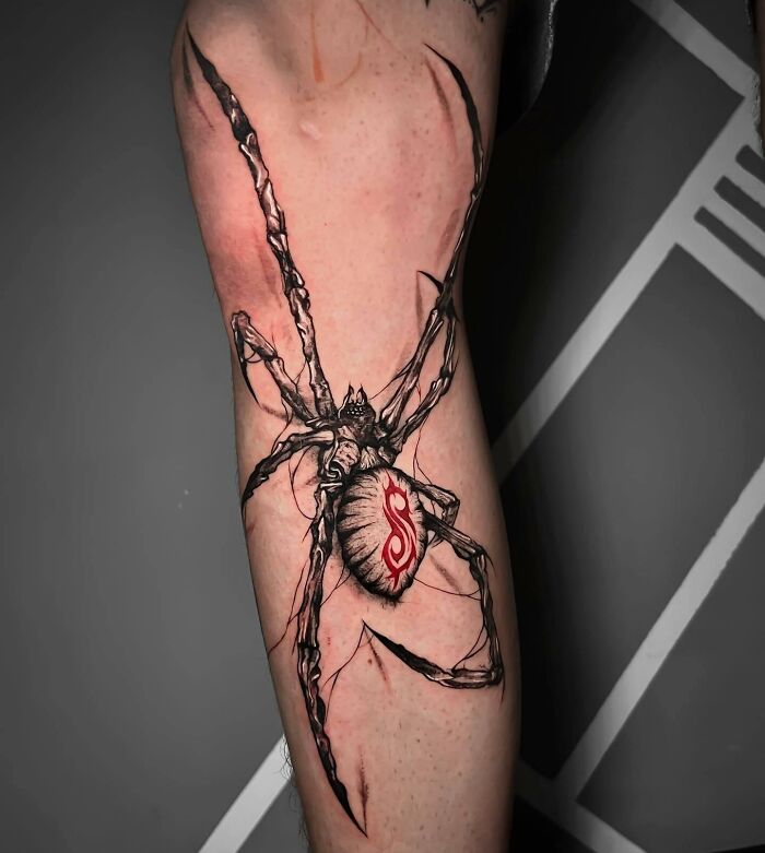 Trash Polka tattoo featuring a black and red spider design on a person's leg.