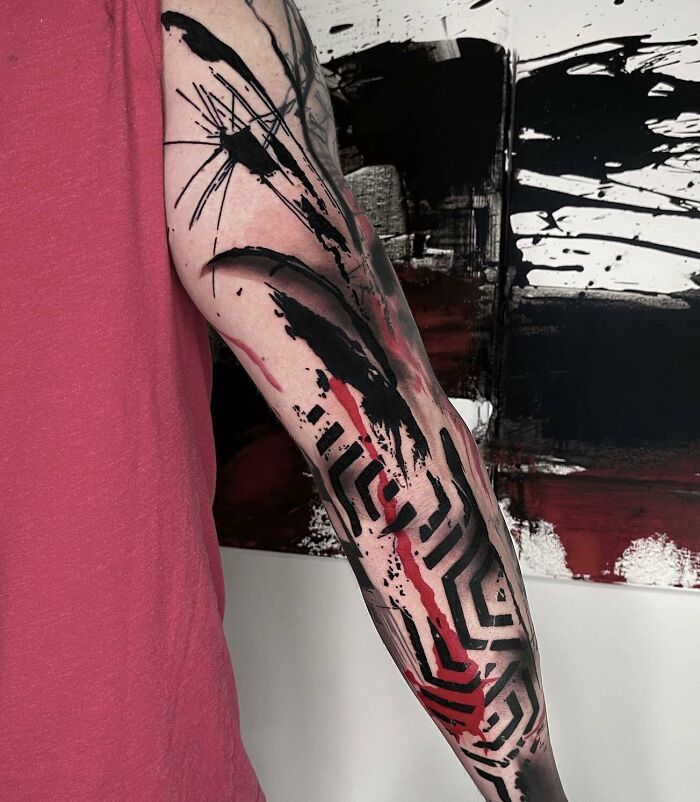 Arm showcasing a bold Trash Polka tattoo design with abstract black and red ink patterns.