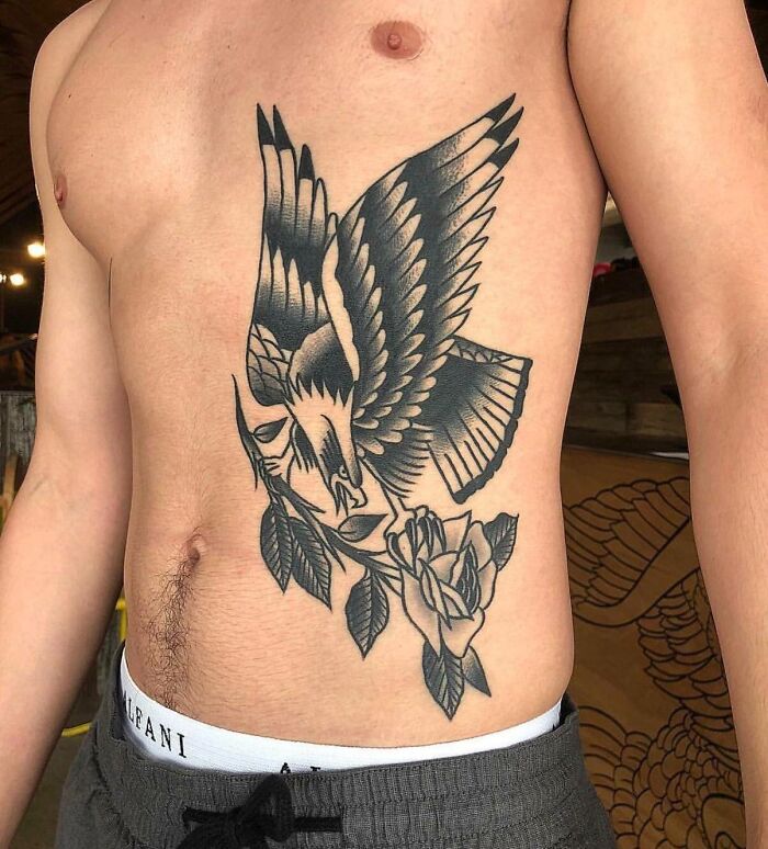 American traditional tattoo of an eagle holding a rose on a person's ribcage.