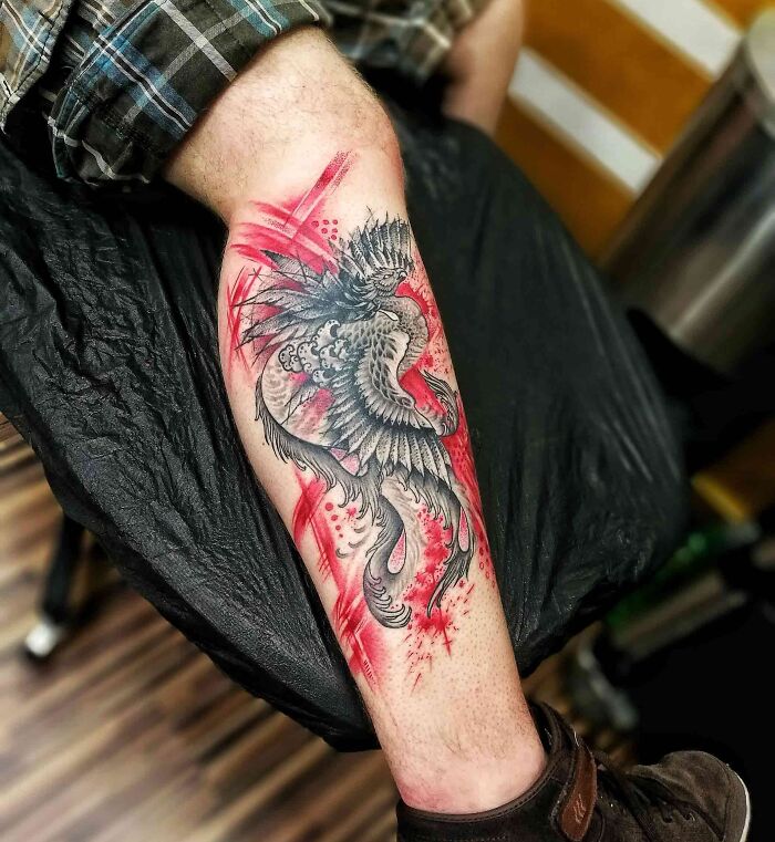 Leg with a detailed trash polka tattoo of a bird, blending black and red ink for a striking design.