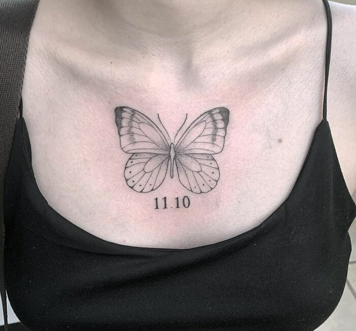 A black and white butterfly tattoo on a person's chest, with the date 11.10 below it.