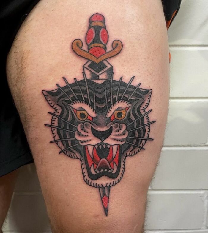 American traditional tattoo of a fierce black animal with a dagger on someone's leg.