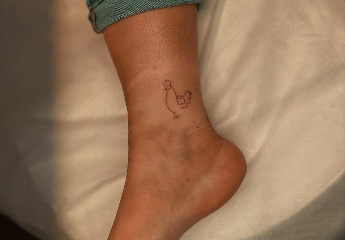 Minimalistic rooster ankle tattoo on a person’s foot, with jeans slightly rolled up.