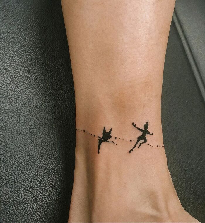 Ankle tattoo of Peter Pan and Tinker Bell silhouettes, connected by a dotted line.