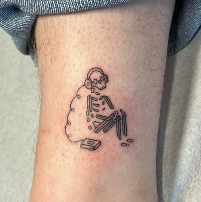 Music tattoo of a skeleton with headphones and a cassette tape on the ankle.