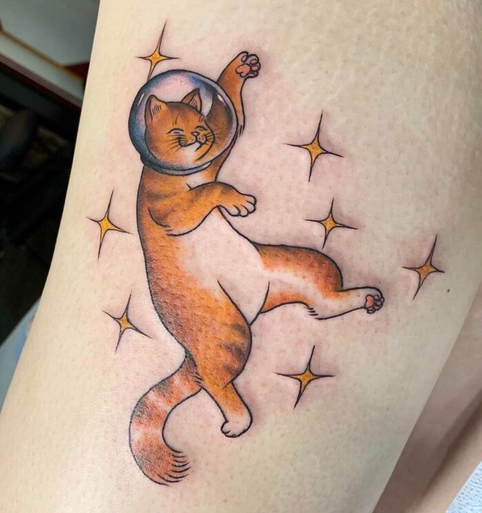 Cat in space helmet tattoo with stars, showcasing cool space-themed body art.