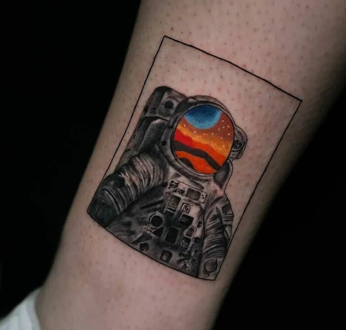 Astronaut tattoo with colorful space helmet on forearm, featuring cosmic landscape design.