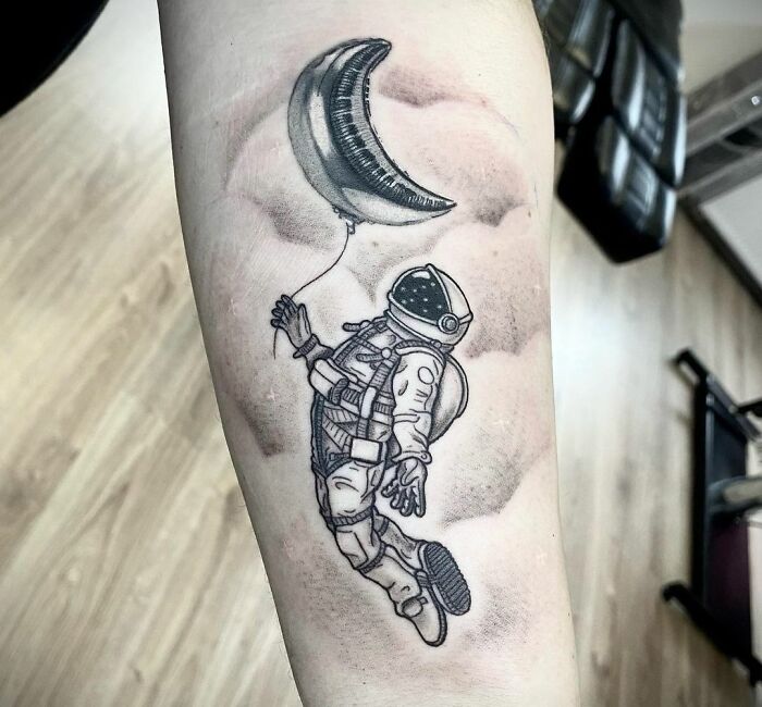 Tattoo of an astronaut floating with a crescent moon balloon, showcasing cool space tattoo art.