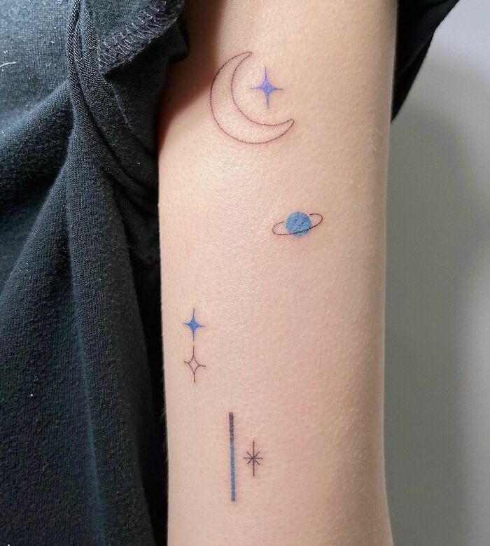 Minimalist space tattoos featuring a crescent moon, stars, and planet on an arm.