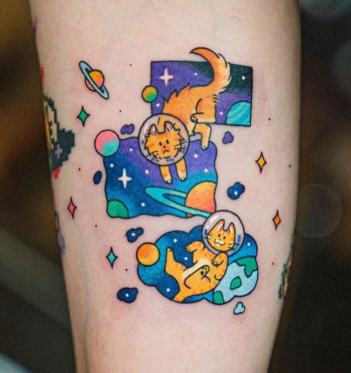 Cosmic-themed tattoo featuring playful cats in space helmets alongside colorful planets and stars.