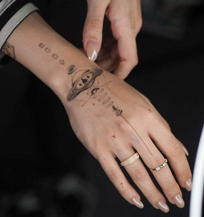 Hand featuring a cool space tattoo of a planet with rings and geometric elements.