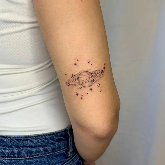 Space tattoo of Saturn with stars on a person's arm, showcasing minimalist cosmic art.