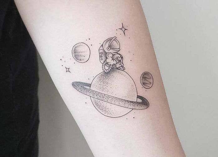 Space tattoo featuring an astronaut on a ringed planet with stars and smaller planets in the background.
