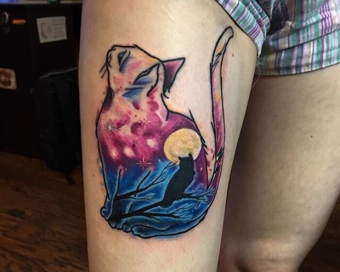 Cosmic cat tattoo with a vibrant space design and moon on a person's thigh.