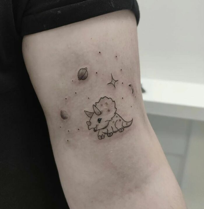 Cute space tattoo of a triceratops with planets and stars on an arm.