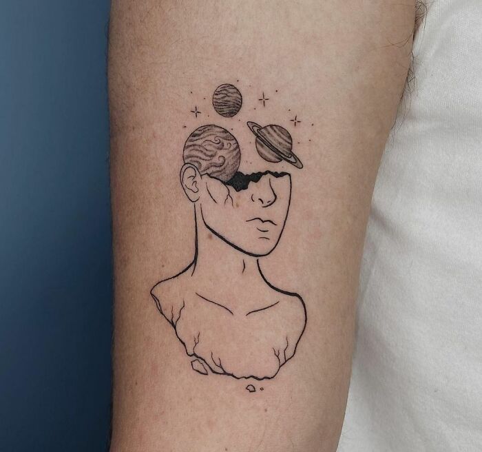 Tattoo of a faceless bust with planets emerging from the head, illustrating a cosmic theme.