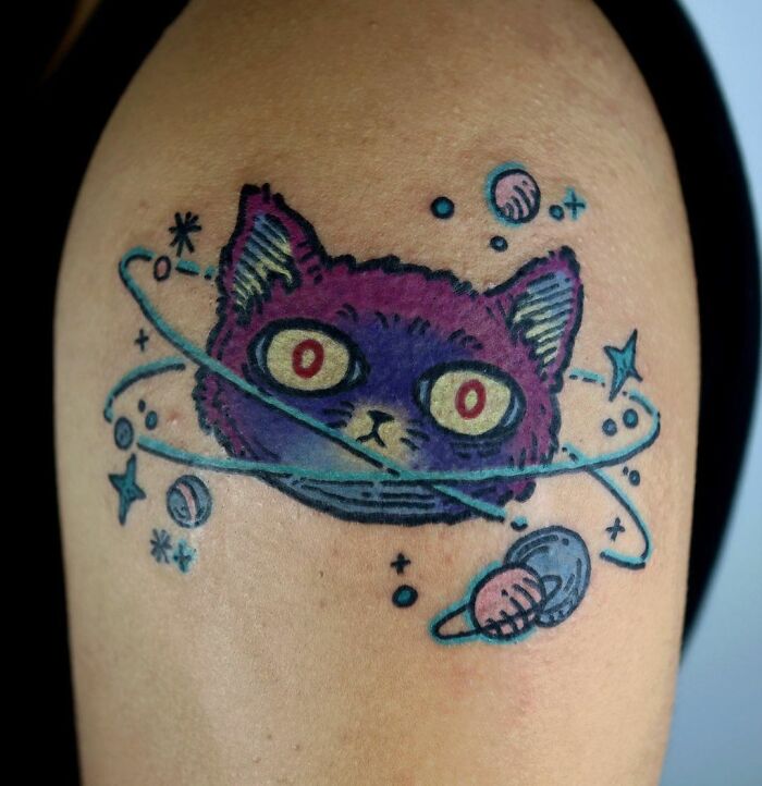 Colorful cat in space tattoo on arm with planets and stars, featuring cool space-themed cosmic design.