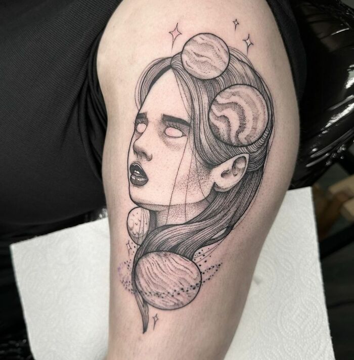 Cosmic tattoo on arm featuring a surrealistic woman's face and planets integrated into the design.