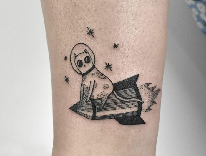 Cat in a space suit tattoo riding a rocket with stars around, featuring cool space-themed body art.