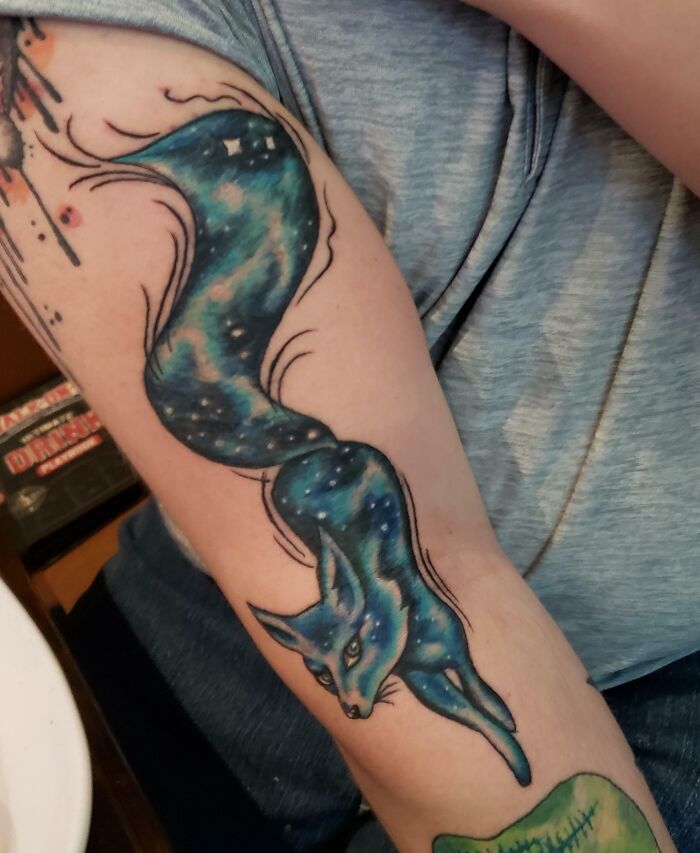 A cool space tattoo of a cosmic fox with starry fur on a person's arm.