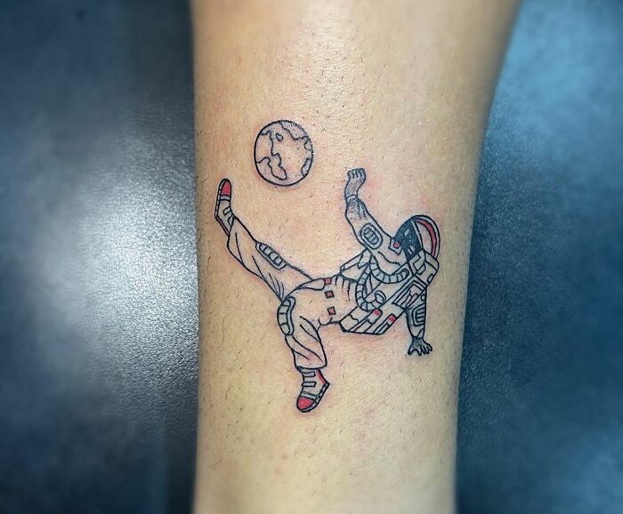 Space tattoo of an astronaut kicking at a moon, creatively inked on forearm.