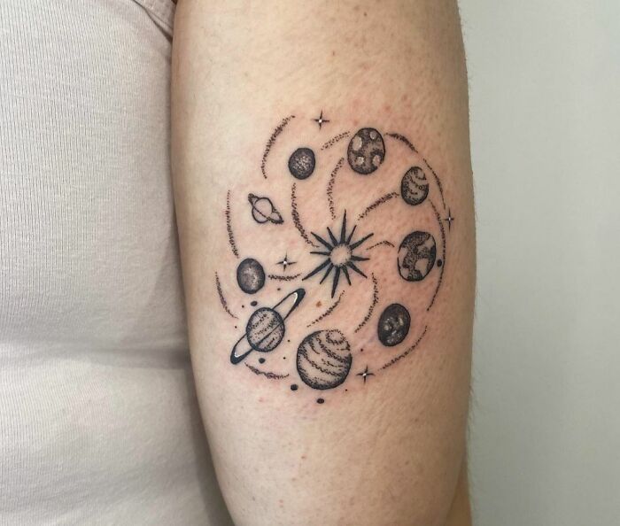 Cosmic space tattoo featuring planets and stars in a swirling pattern on a person's arm.