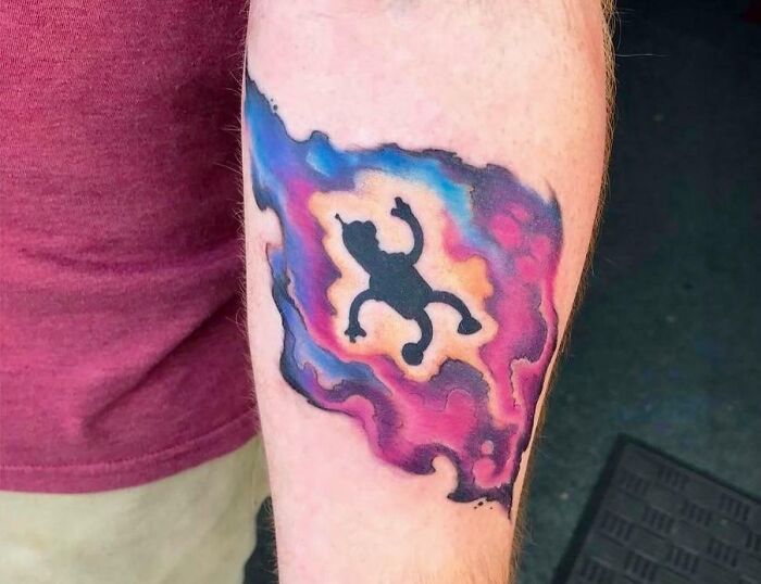 Colorful space tattoo featuring a black alien silhouette with vibrant nebula-like background on an arm.