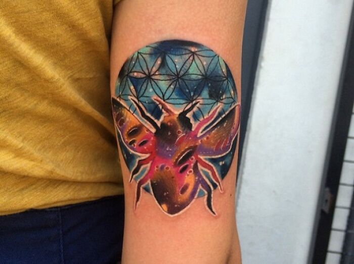 Colorful space tattoo of a beetle on a forearm, featuring cosmic patterns and vibrant galaxy hues.