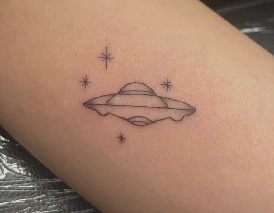 Space tattoo featuring a UFO with small stars, inked on skin.