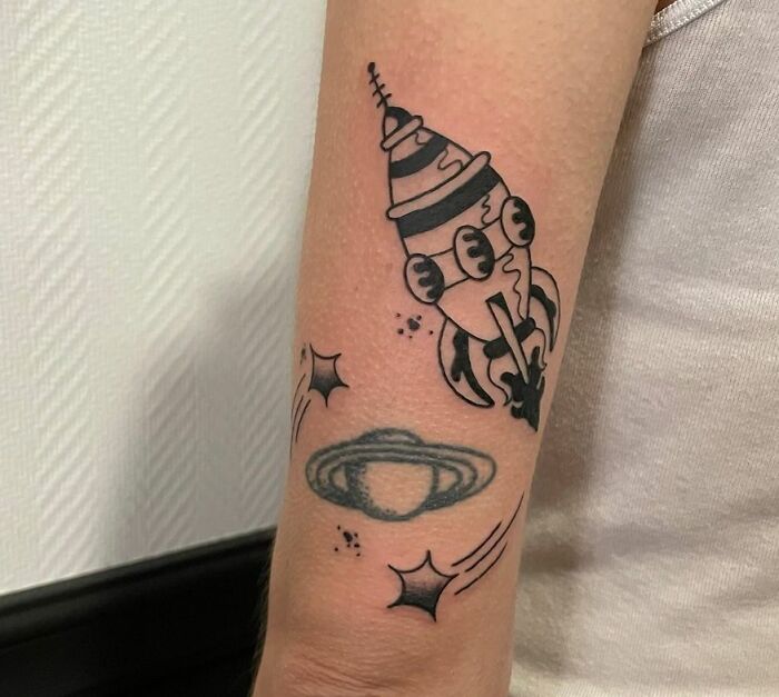 Tattoo of a rocket and planet on arm, featuring cool space theme elements.