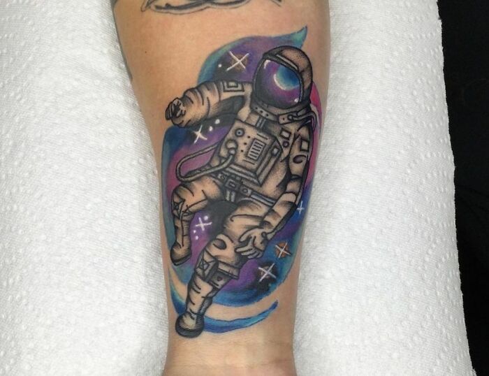 Astronaut space tattoo on arm with colorful cosmic background.
