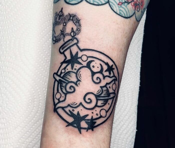 Black ink cosmos tattoo with clouds and stars on an arm.