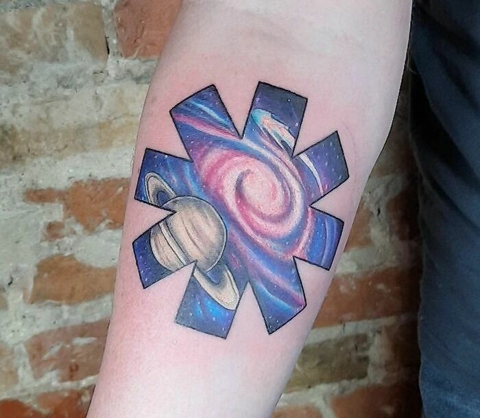 Cool space tattoo featuring a galaxy and Saturn on an arm, against a brick wall background.