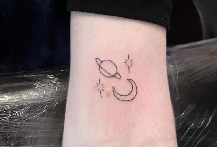 Simple space tattoo featuring a planet, crescent moon, and stars on forearm.