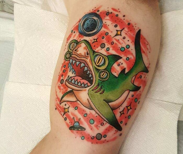 Colorful space tattoo featuring a cartoon shark with alien eyes, surrounded by planets and stars.