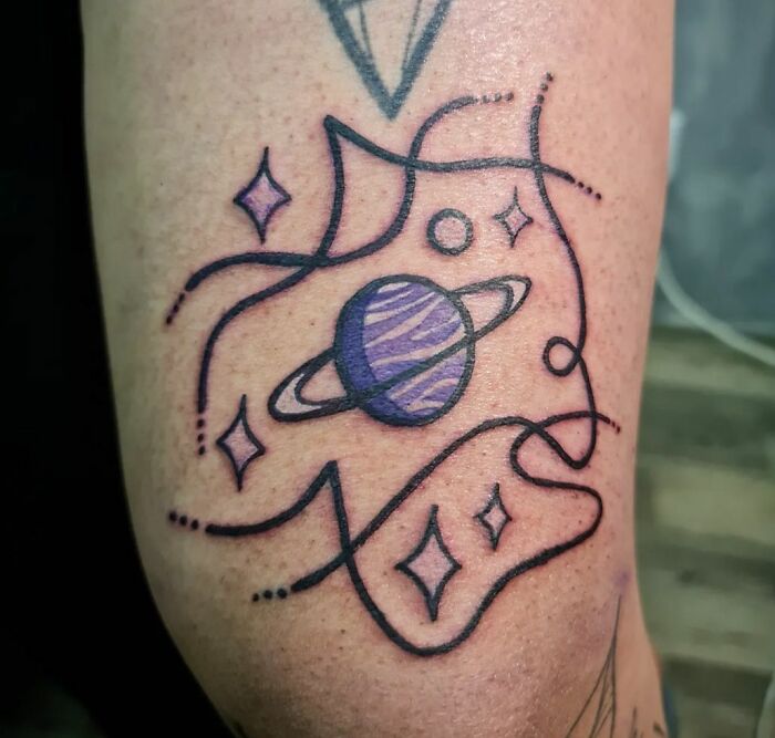Tattoo of a purple planet with rings and stars, showcasing a cool space theme on the skin.