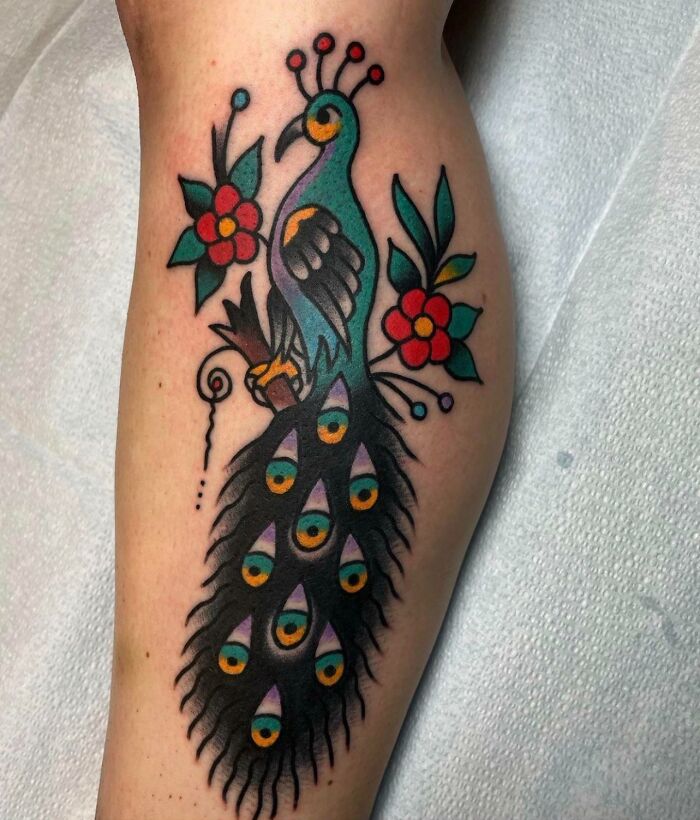 A colorful peacock American traditional tattoo design with flowers on an arm.