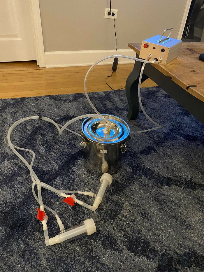 Mysterious object with tubes, valves, and metal container connected to a device on a wooden table on carpeted floor.