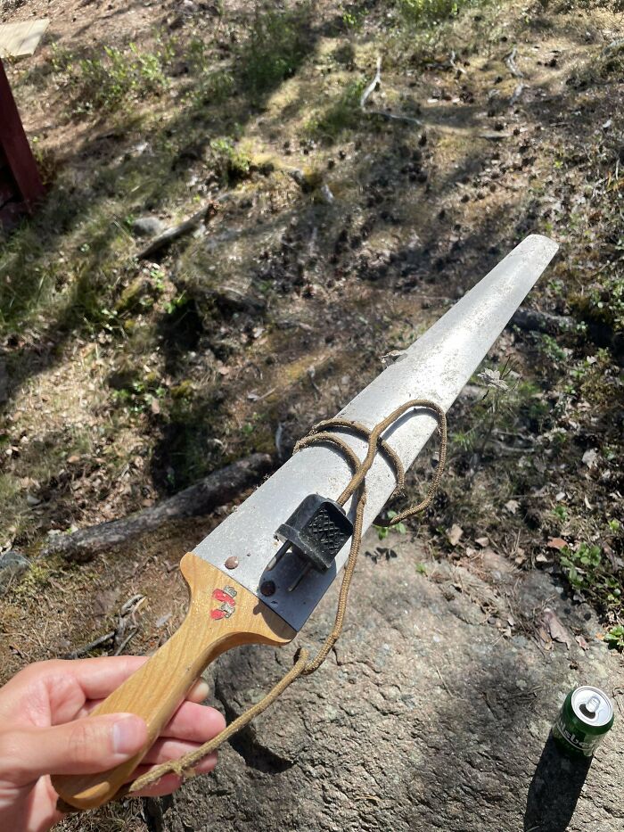 Hand holding a mysterious object with a wooden handle and a long metal blade found outdoors in a natural setting.