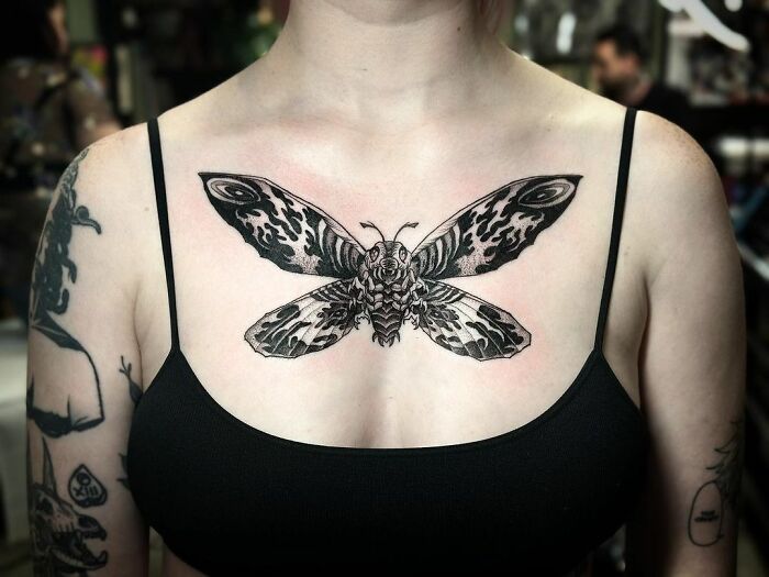 A detailed black moth on chest, showcasing gothic tattoo art on a person in a black top.