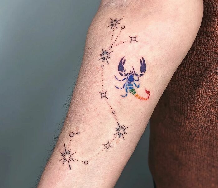 Scorpio zodiac tattoo featuring a colorful scorpion and starry constellation on an individual's arm.