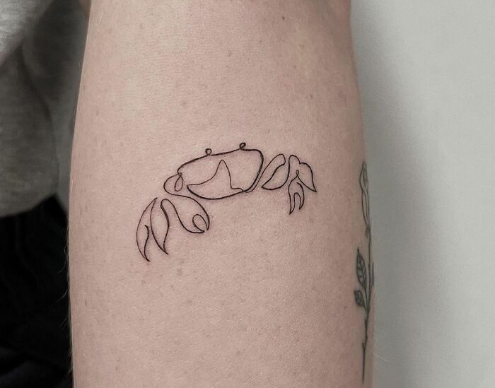 Minimalist zodiac tattoo of a crab on an arm, representing the Cancer sign.