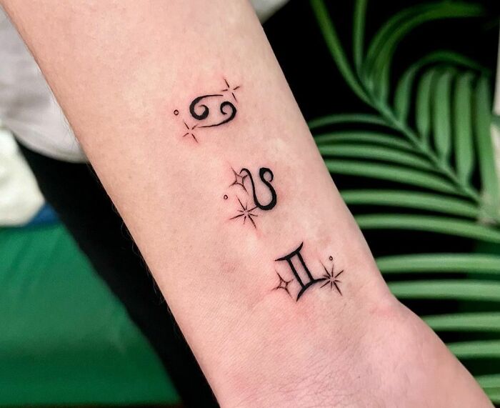 Stylish zodiac tattoos featuring Cancer, Leo, and Gemini symbols on a forearm.