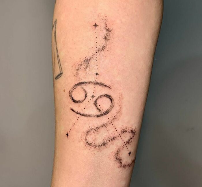 Zodiac tattoo featuring the Cancer symbol with starry details on an arm.